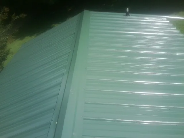 New green metal panels meeting at the ridge of a roof — Flat Roof Repair work by our crew in Tipton