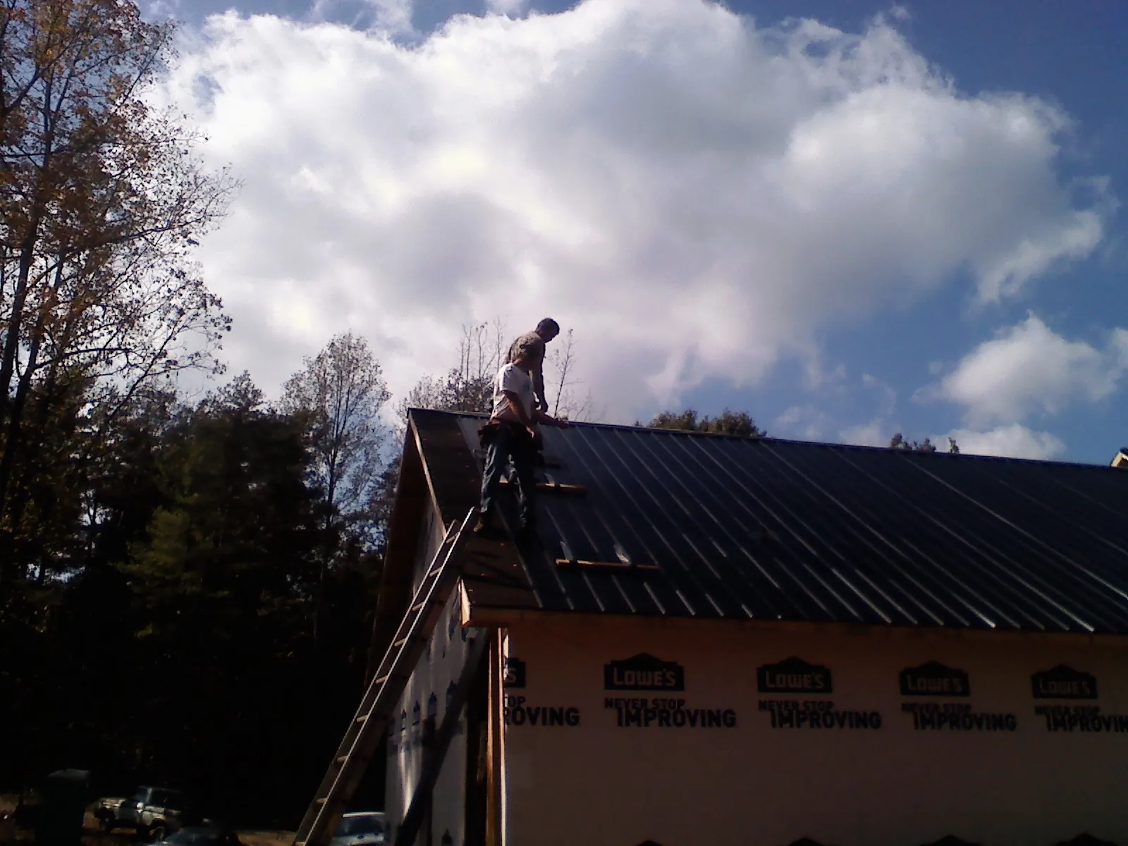 Roofer fastening dark metal panels high against a cloudy sky, from a Roof Inspection job in Tipton