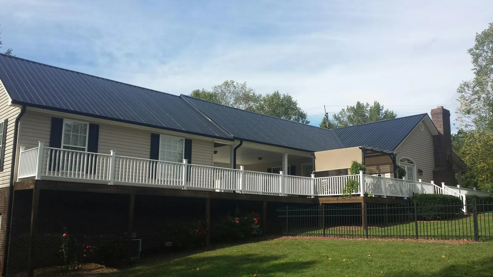 Black metal roof above a long white railed deck on a hillside home in Tipton
