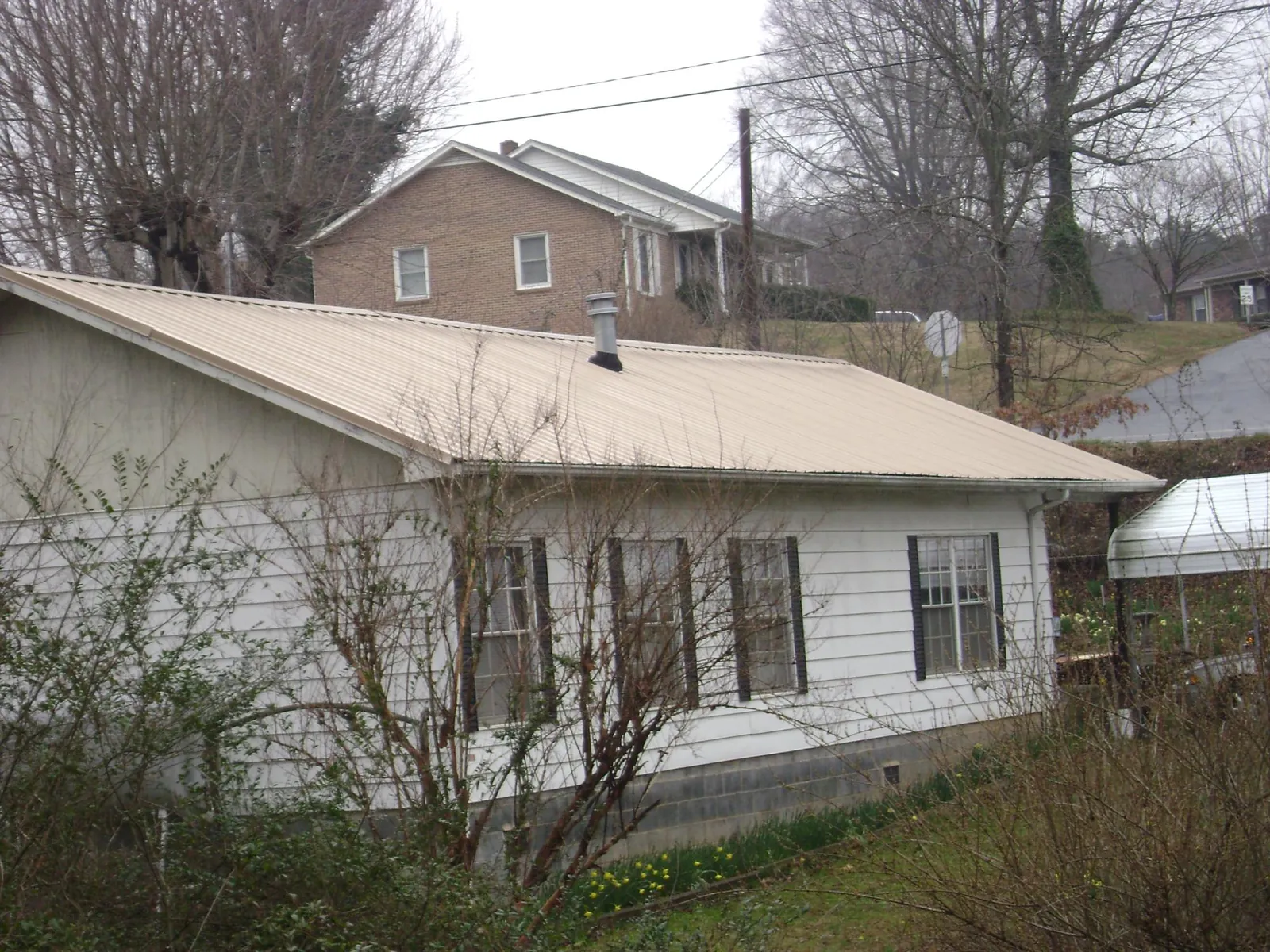 Tan metal roof on a white sided house set into a hillside — Commercial Roofing by Roofing Brothers in Tipton